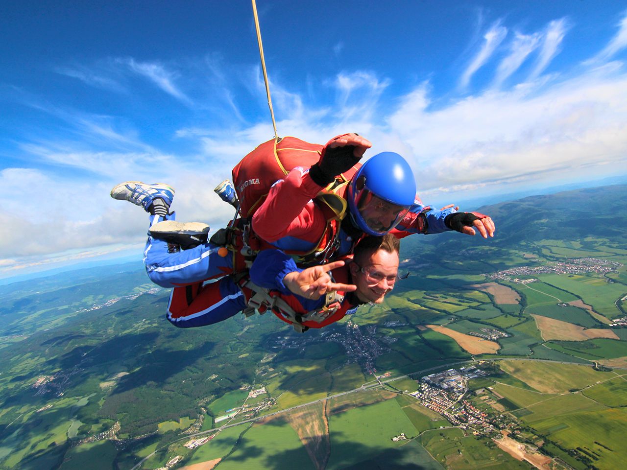 Tandempilot a nadšený pasažier počas voľného pádu pri tandemovom zoskoku s padákom – adrenalínový zážitok v oblakoch.